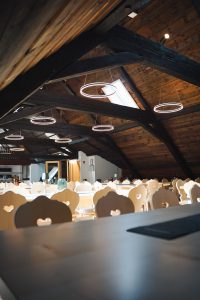 Blick an die dunkle Holzdecke des Raumes, die den Kontrast zwischen dem rustikalen Gebälk und den schlichten, leuchtenden LED-Ringen der Hängelampen betont.