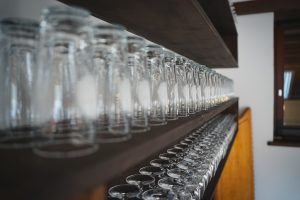 Nahaufnahme von zahlreichen sauberen Gläsern, die ordentlich aufgereiht auf mehreren Ebenen eines Holzregals stehen.