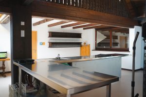 Eine professionelle, leere Gastro-Theke mit Edelstahlarbeitsflächen und hölzernen Wandregalen im Hintergrund.